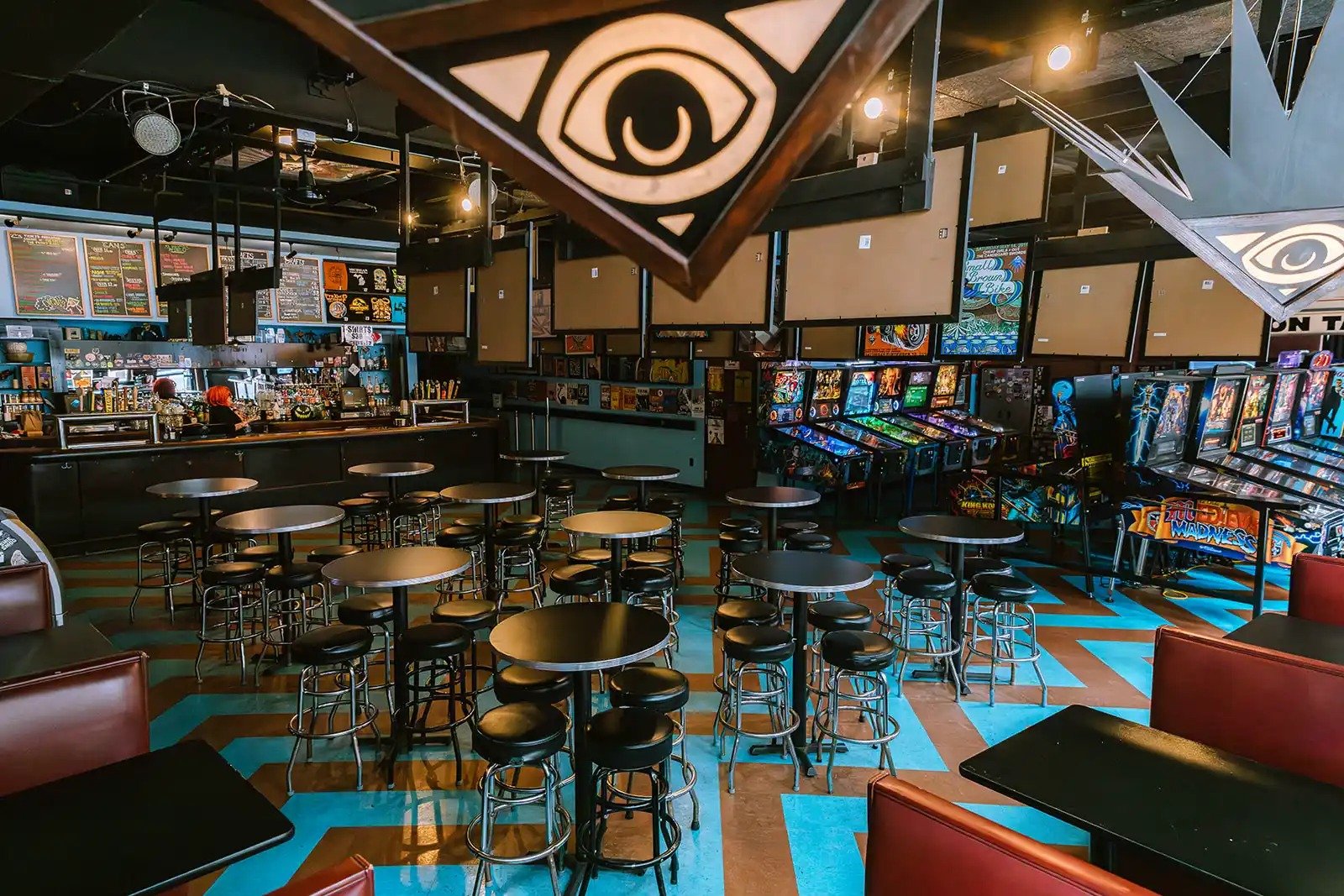 Pyramid Scheme — the bar room with its eye-pyramid signs, high tables and pinball row